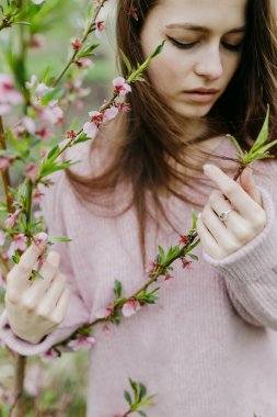 İlkbaharda çiçek açan bir bahçede çiçek açan güzel bir Avrupalı kızın dikey portresi