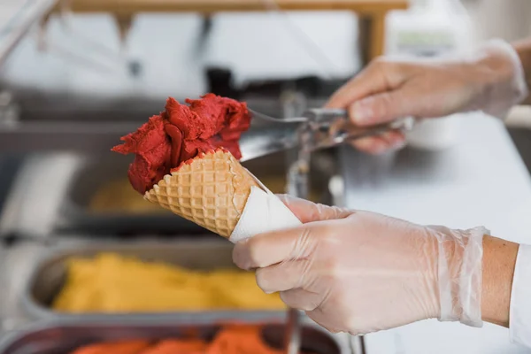 在华夫饼杯里的冰淇淋。草莓冰激凌。冰淇淋制造商在夏天做冰淇淋.卖冰淇淋的人的手. 图库照片