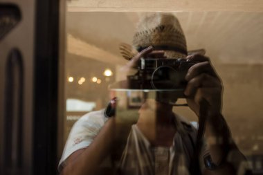 Elinde retro kamera olan bir turist dükkan camının yansımasından selfie çeker..