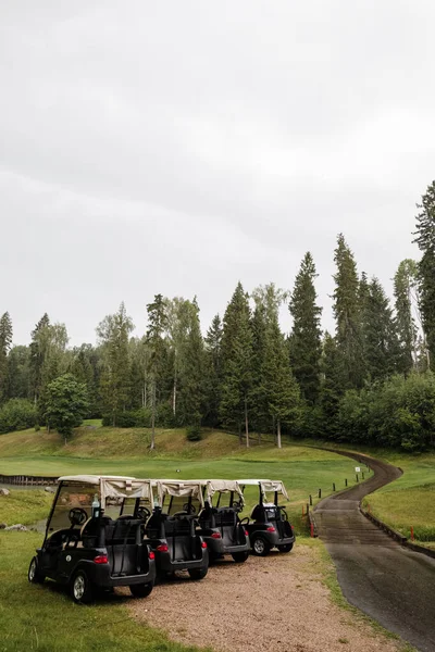Four golf carts and a scenic view. Forest, golf club, green grass, cloudy weather.