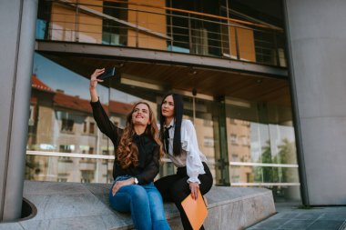 İki güzel beyaz iş kadını şirketin önünde dikilip telefonu kullanırlar. İş ve teknoloji