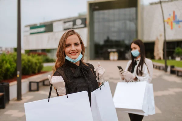 バッグを持ったショッピングセンターの前には マスクと手袋をした2人の美しい白人女性が立っています ショッピングとウイルス保護 Covid — ストック写真
