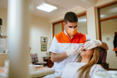 Genç dişçi dişlerini incelerken güzel beyaz bir kadın dişçinin ofisinde bir sandalyede oturuyor.