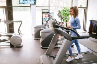 Güzel bir beyaz kız spor salonunda koşu bandında koşuyor.