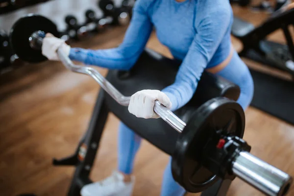 Spor salonunda ağırlıkları olan koruyucu maskeli beyaz bir kadın.