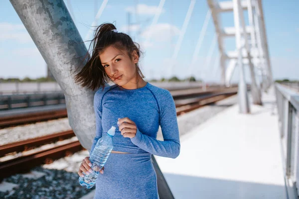 Mavi Spor Ekipmanları Içinde Elinde Bir Şişe Suyla Köprüde Genç — Stok fotoğraf