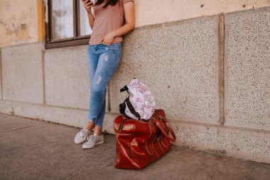 Eski tren istasyonunda hasır şapkalı, sırt çantalı ve elinde telefon olan güzel bir genç kadın.