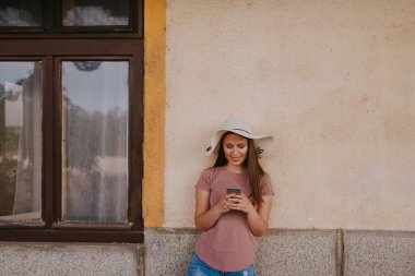 Eski tren istasyonunda hasır şapkalı, sırt çantalı ve elinde telefon olan güzel bir genç kadın.