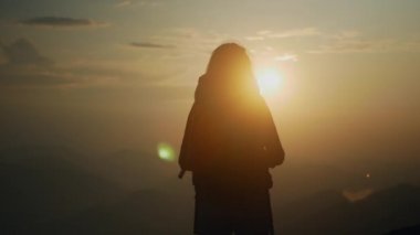 Sırt çantalı kız dağın zirvesinde gün batımını izliyor