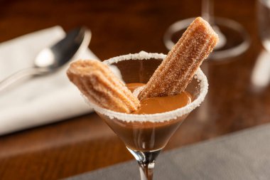 Mini churros ve dulce de leche tatlısı bulanık bir arka planda bir bardak üzerinde kaşık ve cam şarapla