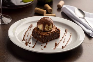 Dondurmalı çikolatalı Brownie, beyaz tabak, şarap sürahisi mantarı ve peçeteli.
