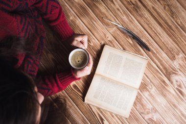 bir fincan kahve ve okuma tutan bir kırmızı kazaklı genç kadın