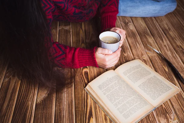 Молодая женщина в красном свитере держит чашку кофе и читает — стоковое фото