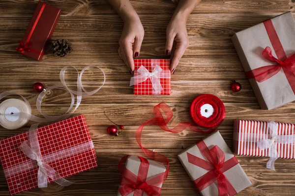Female hands wrapping xmas gifts into paper and tying them up with red and white threads