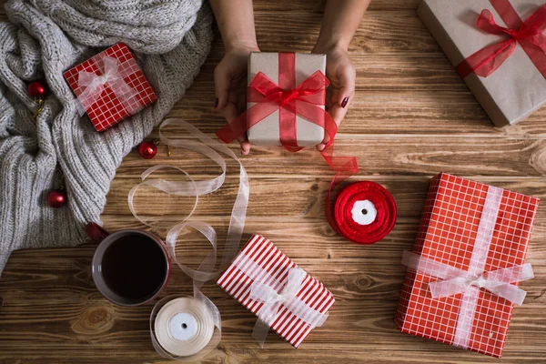 Γυναικεία χέρια περιτύλιγμα χριστουγεννιάτικα δώρα σε χαρτί και δένοντας τους με κόκκινες και άσπρες κλωστές Φωτογραφία Αρχείου