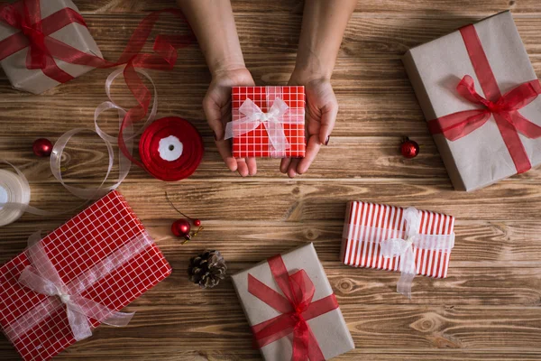 Γυναικεία χέρια τυλίγοντας Χριστούγεννα δώρα σε χαρτί και δένοντας τους με κόκκινες και άσπρες κλωστές Φωτογραφία Αρχείου