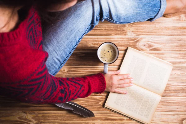 Молодая женщина в красном свитере держит чашку кофе и читает — стоковое фото