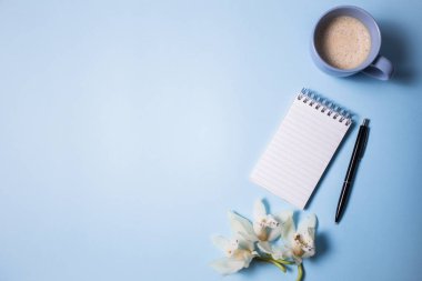 Fincan kahve ve defter ile mavi arka plan, üstten görünüm üzerinde kalem ve orkide çiçek