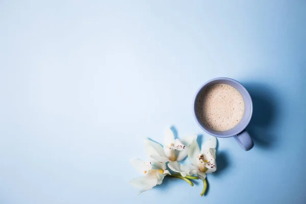 Filiżankę kawy i Orchidea kwiat na niebieskim tle — Zdjęcie stockowe