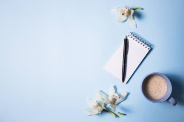 Fincan kahve ve defter ile mavi arka plan, üstten görünüm üzerinde kalem ve orkide çiçek