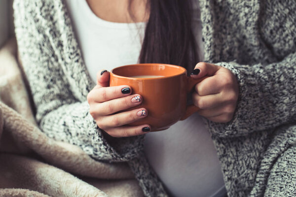 Woman with beautiful manicure holding a orange cup of cocoa