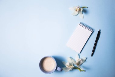 Fincan kahve ve defter ile mavi arka plan, üstten görünüm üzerinde kalem ve orkide çiçek
