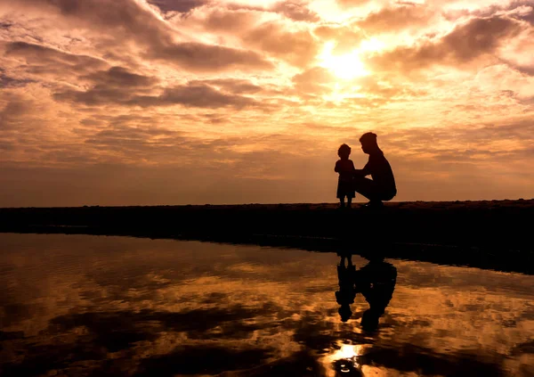 Spiegelung Silhouette der Mutter mit ihrem Kleinkind gegen die Sonne — Stockfoto