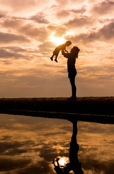 Spiegelung Silhouette der Mutter mit ihrem Kleinkind gegen die Sonne — Stockfoto