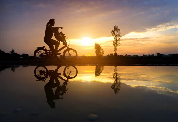 Spiegelung Silhouette der Mutter mit ihrem Kleinkind auf Fahrrad agai — Stockfoto