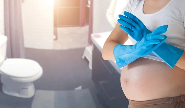 Gravid kvinna som bär blå handskar städningen av toaletten. — Stockfoto