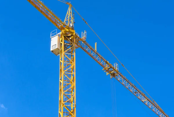 Yellow construction tower crane against blue sky