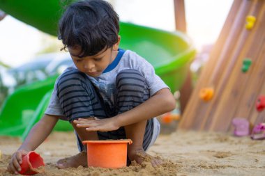 Asyalı bir çocuk oyun oynuyor, oyun alanında kum kazıyor..