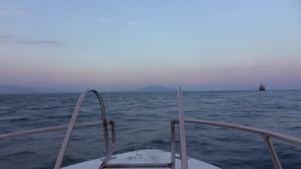 船の船首からの眺め 日没や夜明けに開かれた海の中でボートをピッチ 2匹のイルカが水から飛び出て波に姿を消します 嵐の始まりだ 水平線上の大型船 — ストック動画
