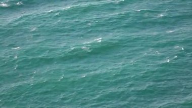 Turkuaz dalgalar okyanusun yüzeyinde. Mavi suda beyaz köpük görünür ve kaybolur. Güçlü deniz üzerinde yukarıdan sabit bir manzara