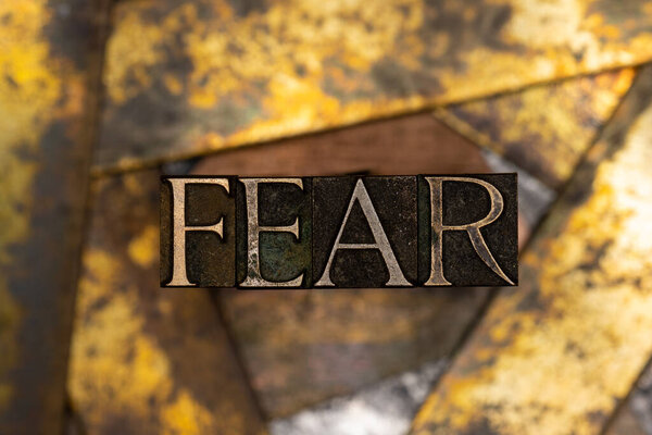 Photo of real authentic typeset letters forming Fear text on vintage textured grunge copper and black background 