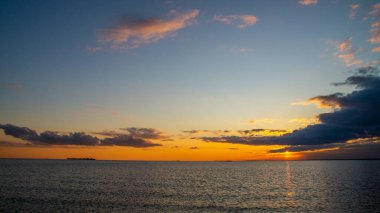 Deniz kıyısında gün batımı, kumsal, dramatik bulutlar.