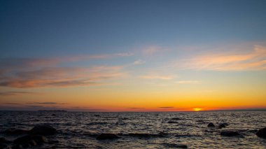 Denizin kumlu sahilinde gün batımı, pembe bulutlar, kayalar.