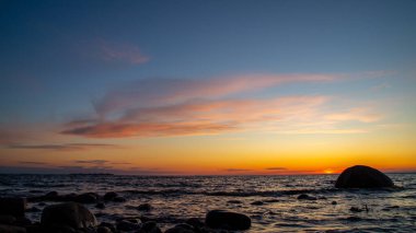 Deniz kıyısında gün batımı, pembe bulutlar, kayalar..