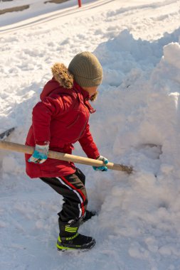 Çocuk bahçede kar temizliyor.