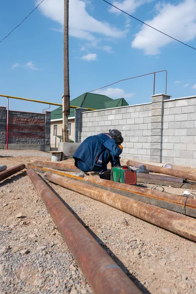 worker welds a rusty pipe in the street in the yard of the plant