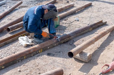 İşçi fabrikanın bahçesindeki sokakta paslı bir boruyu kaynaklıyor.