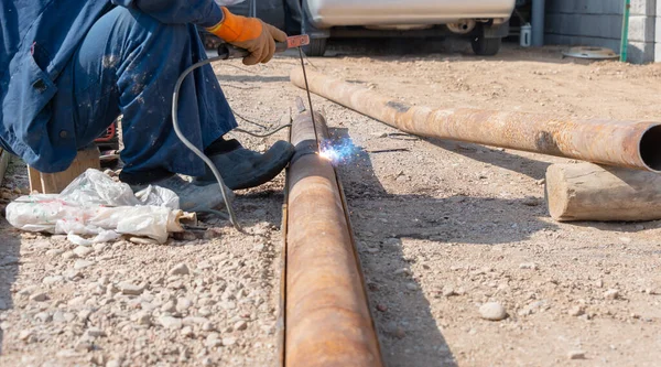 İşçi fabrikanın bahçesindeki sokakta paslı bir boruyu kaynaklıyor.