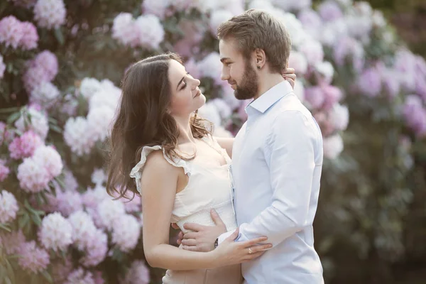 一对年轻夫妇的爱情故事 一个男人和一个女人拥抱在一起 站在英格兰的一个杜鹃公园里 在粉色开花的灌木和树木后面 女人穿白色上衣 男人穿浅蓝色衬衫 在公园里跳舞 — 图库照片