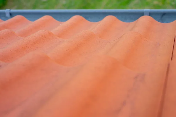 roof tiles and gutter view from above from the roof. brown roof tiles. rain gutter on the roof and view of green meadow