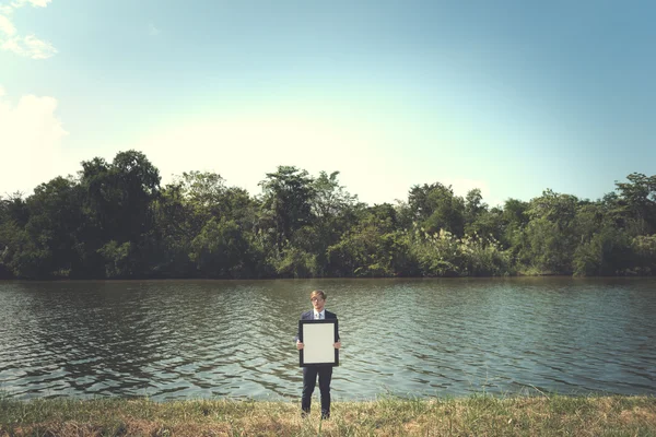 Homme d'affaires avec planche vide debout au bord de la rivière — Photo