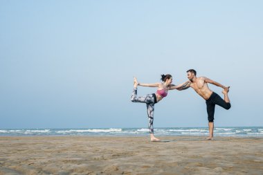 Çiftler plajda yoga yapıyor.