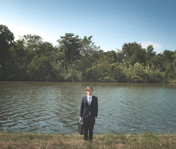 Businessman with briefcase at the river — Stock Photo, Image