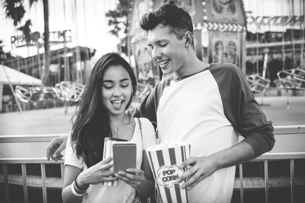 Pareja usando móvil en parque de atracciones —  Fotos de Stock