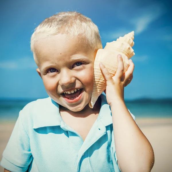 Little Boy ouvindo shell na praia — Fotografia de Stock