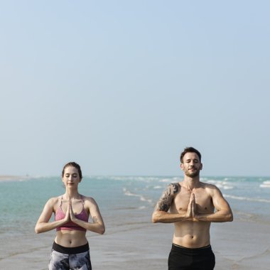 Çiftler plajda yoga yapıyor.